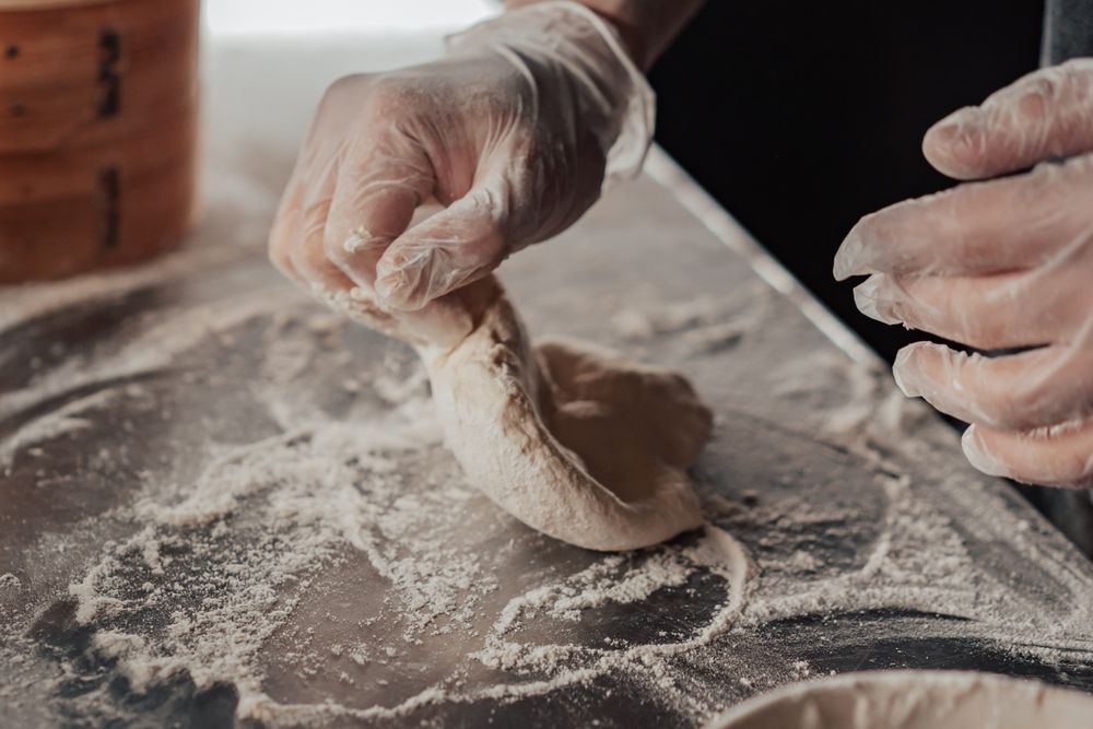 A baker shaping dough on a flour-dusted work surface.